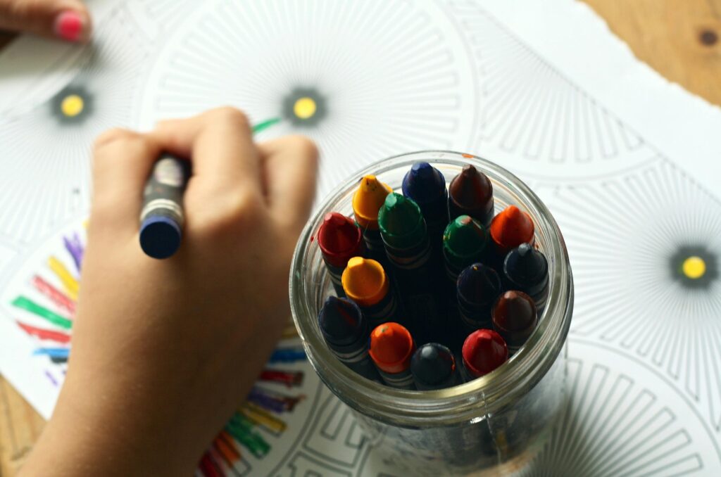 A child drawing with colorful crayons, fostering creativity and fun in a learning environment.