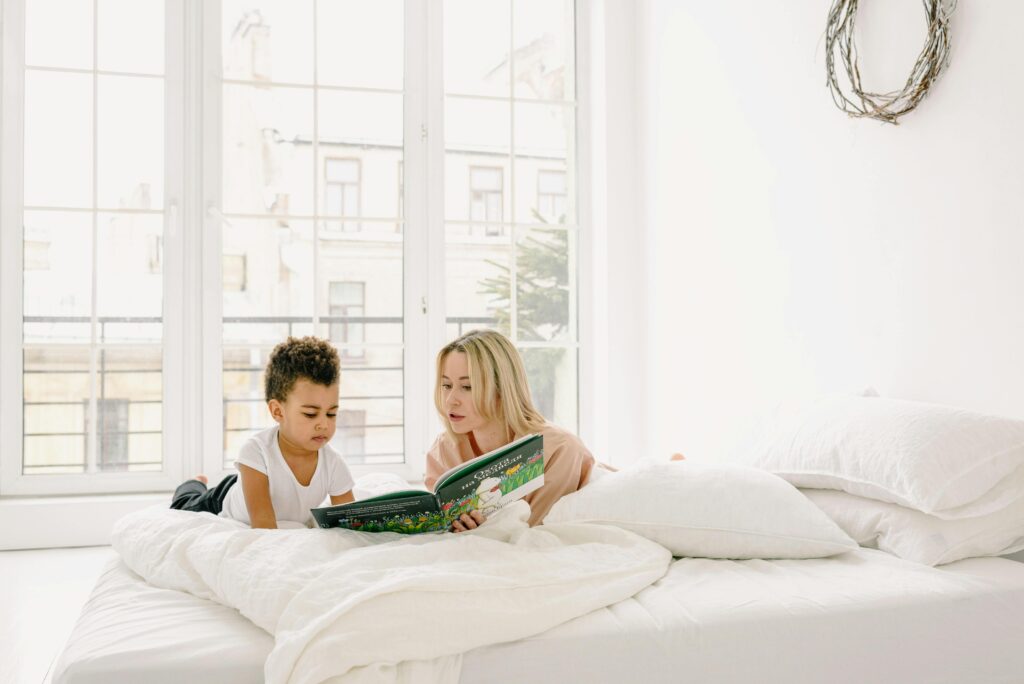 A mother and son enjoy reading together in a sunlit bedroom, fostering family bonding.
